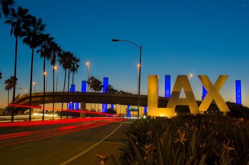 Illuminated LAX sign with palm trees and colorful columns at dusk.